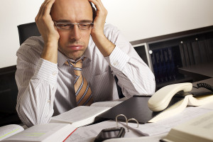 Stressed businessman sitting at desk in office being overloaded